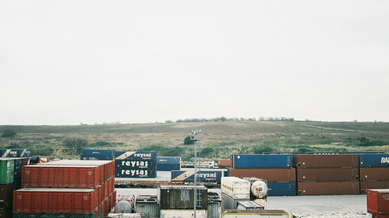 Rows of stacked ocean shipping containers and tank containers of various carriers sitting in a container storage yard.