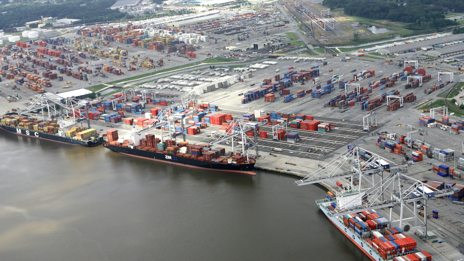 Aerial view of the Port of Savannah container terminal on the Savannah River, with docked container ships, ship-to-shore cranes, stacked ocean containers, and an intermodal rail yard.